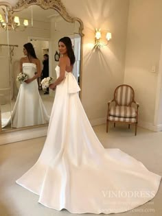 a woman standing in front of a mirror wearing a wedding dress with bow at the waist