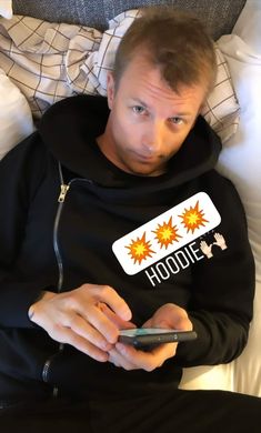 a man in a hoodie looking at his cell phone while laying on a bed