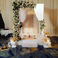 an altar decorated with flowers and greenery in front of a white drape curtain