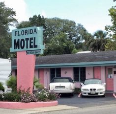 two cars parked in front of a motel with pink walls and palm trees behind it