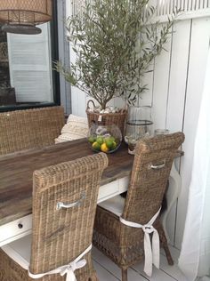 wicker chairs around a table with fruit on it and an olive tree in the background