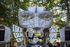 a group of people standing in front of a white sculpture with multiple faces on it