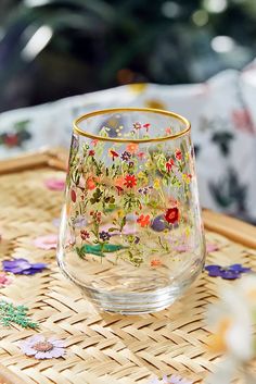 a glass with flowers painted on it sitting on a wicker tray next to a christmas tree