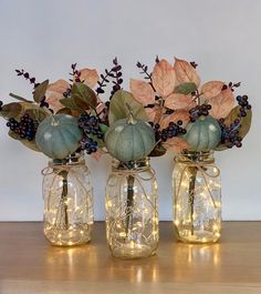 three mason jars filled with pumpkins, berries and greenery are sitting on a table