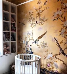 a baby's crib in front of a wall with birds and flowers on it