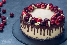 a cake with cherries and chocolate drizzled on top, sitting on a slate platter