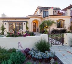 a large house with lots of plants and flowers around it's front entrance area