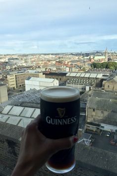 a person holding up a beer in front of a cityscape with the guinness logo on it