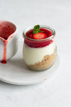 a dessert in a glass jar on a white plate next to a bowl of strawberries