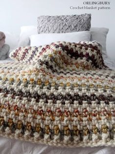 a crocheted blanket sitting on top of a bed next to pillows and blankets