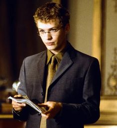 a young man in a suit and tie holding a piece of paper while looking at the camera