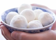 a person holding a blue and white bowl filled with small balls of doughnuts