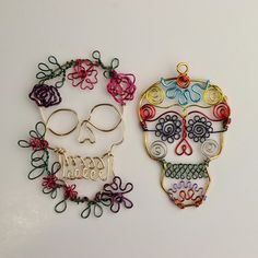 two colorful sugar skulls are next to each other on a white surface, one is made out of wire and the other has scissors