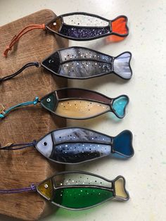 five fish shaped glass ornaments sitting on top of a wooden board