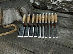 a set of seven wood carving tools sitting on top of a wooden table next to a rope