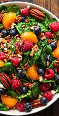 a salad with spinach, oranges, blueberries and pecans in it