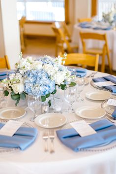 the table is set with blue and white place settings, silverware, and flowers