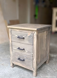 a wooden box with two drawers sitting on top of cement floor next to a wall