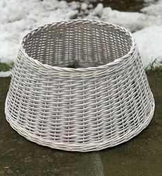 a white wicker basket sitting on the ground in front of some snow covered grass