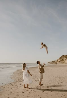 a man and woman on the beach playing with a cat in the air above them