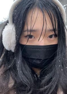 a woman wearing a black face mask and ear muffs in the snow with her hair blowing back