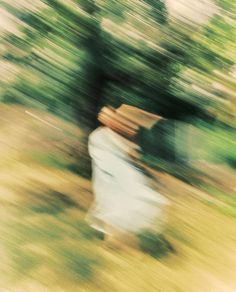 a blurry photo of a person with a hat on walking in the grass and trees