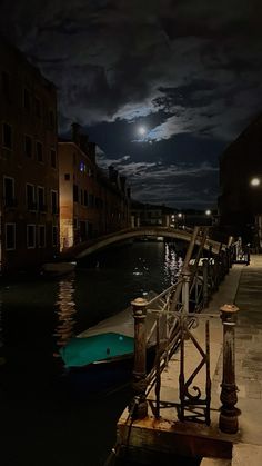 a boat is docked in the water at night with a full moon behind it and buildings on either side