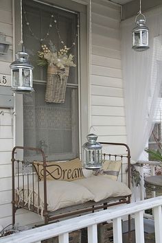 a bed sitting on top of a porch next to a white house with flowers in the window