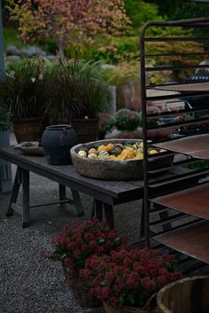 an outdoor table with baskets and flowers in the back ground next to potted plants