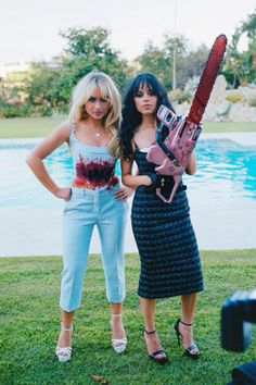 two women standing next to each other in front of a pool with a chainsaw