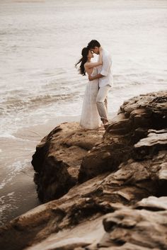 a bride and groom standing on rocks by the ocean