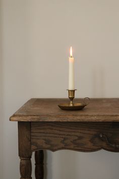 a lit candle is sitting on top of a wooden table with a bowl on it