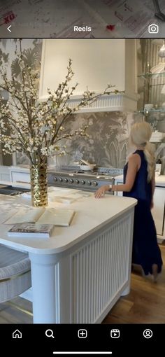 a woman standing in front of a kitchen counter next to a vase filled with flowers