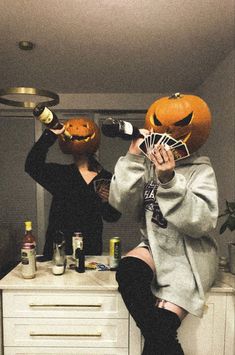 two women in halloween costumes are sitting on a dresser and one woman is holding up an orange jack - o - lantern