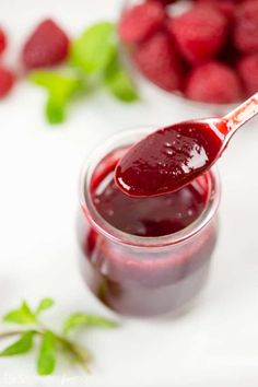 a spoon full of raspberry jam on a white surface with fresh berries in the background