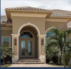 the front entrance to a large home with palm trees and shrubs in front of it