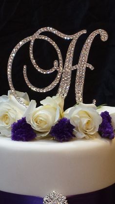 a wedding cake with white roses and purple ribbon on the bottom tier is decorated with an initial monogram