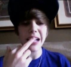 a young boy wearing a black hat and holding his finger to his mouth while sitting on a couch