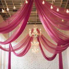 a chandelier hanging from the ceiling in front of a white brick wall and pink drapes