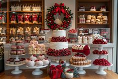 a table topped with lots of cakes and cupcakes next to christmas wreath on the wall