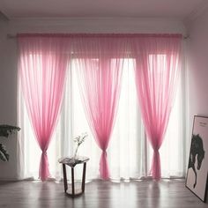 a living room with pink curtains and a table in front of the window, next to a plant