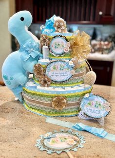 a baby shower cake with a blue dinosaur on top and decorations around the bottom tier