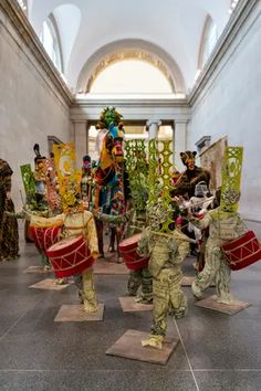 some people are dressed up and playing drums in a room filled with statues, plants and decorations