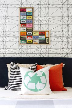 a bed topped with lots of pillows next to a wall covered in cassette tape art