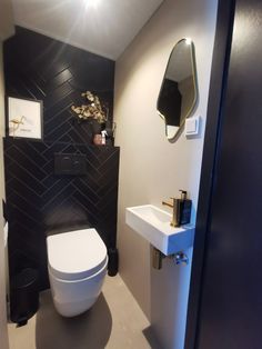 a white toilet sitting in a bathroom next to a sink and wall mounted faucet