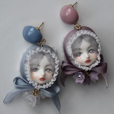 two little dolls with blue eyes are hanging from earrings