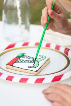 a person holding a green toothbrush in front of a decorated cookie on a plate