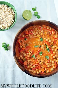 a wooden bowl filled with chickpeas and rice next to a lime slice on the side