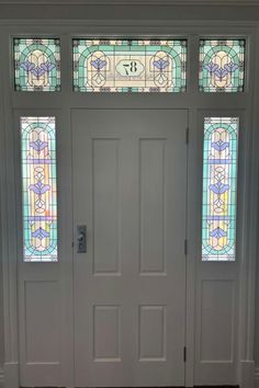 a flower stained glass design installed onto a front door of a home with a hallway. Different sizes stained glass stuck to windows with a central door number.