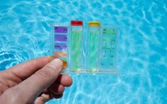 a hand holding two test tubes next to a swimming pool